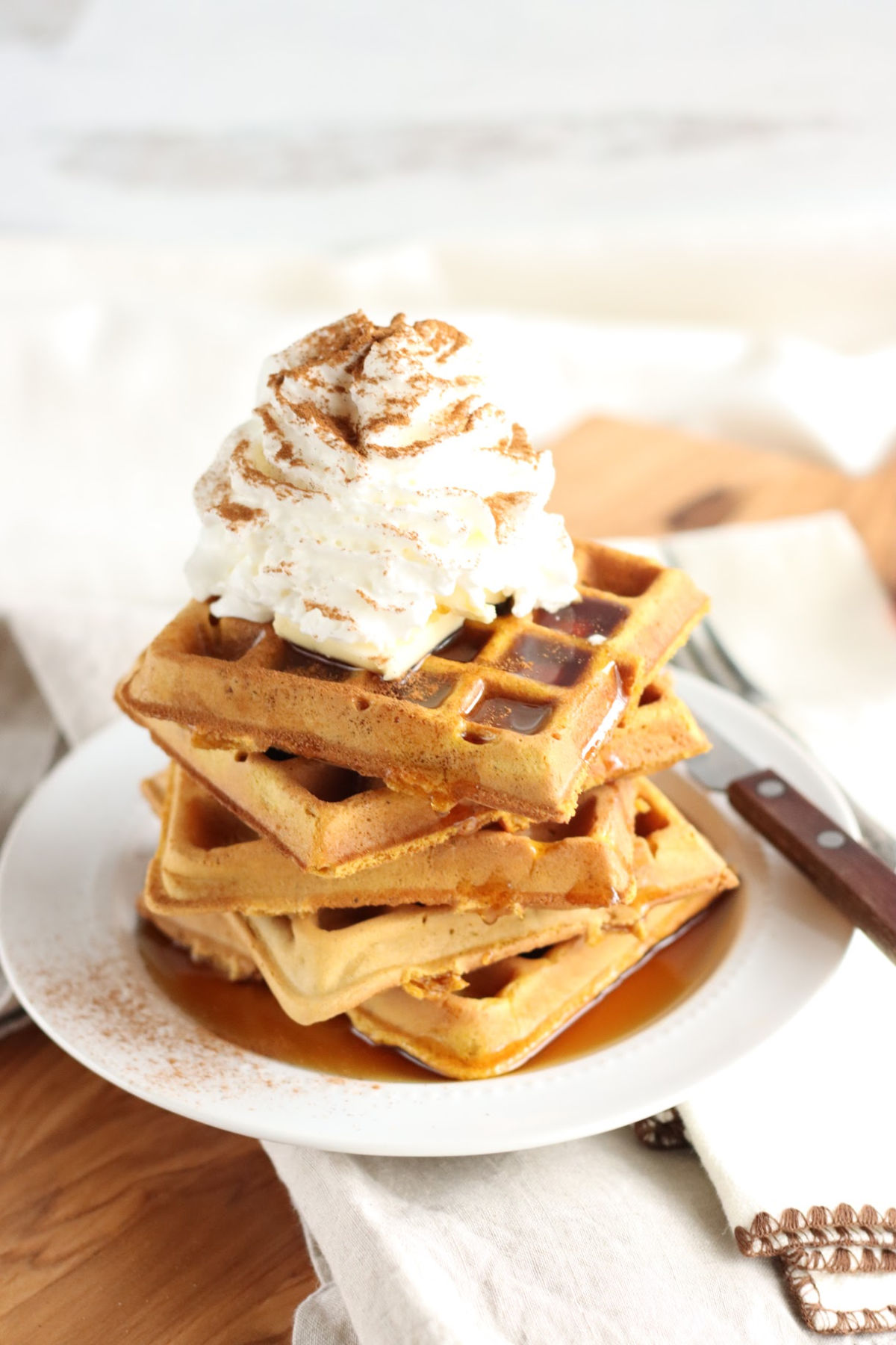 square waffles stacked on each other on small white plate, topped with whipped cream and cinnamon.