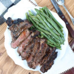 Steak sliced on white plate with fresh green beans.
