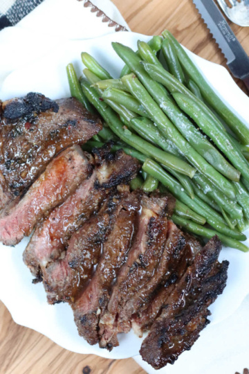 Steak sliced on white plate with fresh green beans.