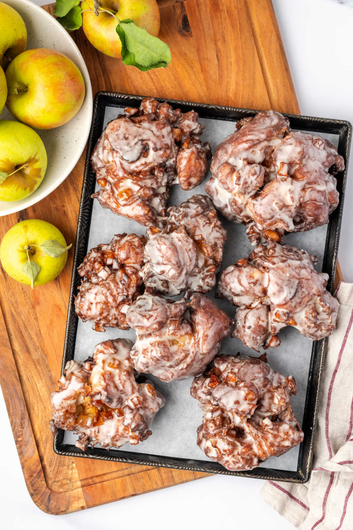 Apple fritters on vintage sheet pan, fresh apples to side.