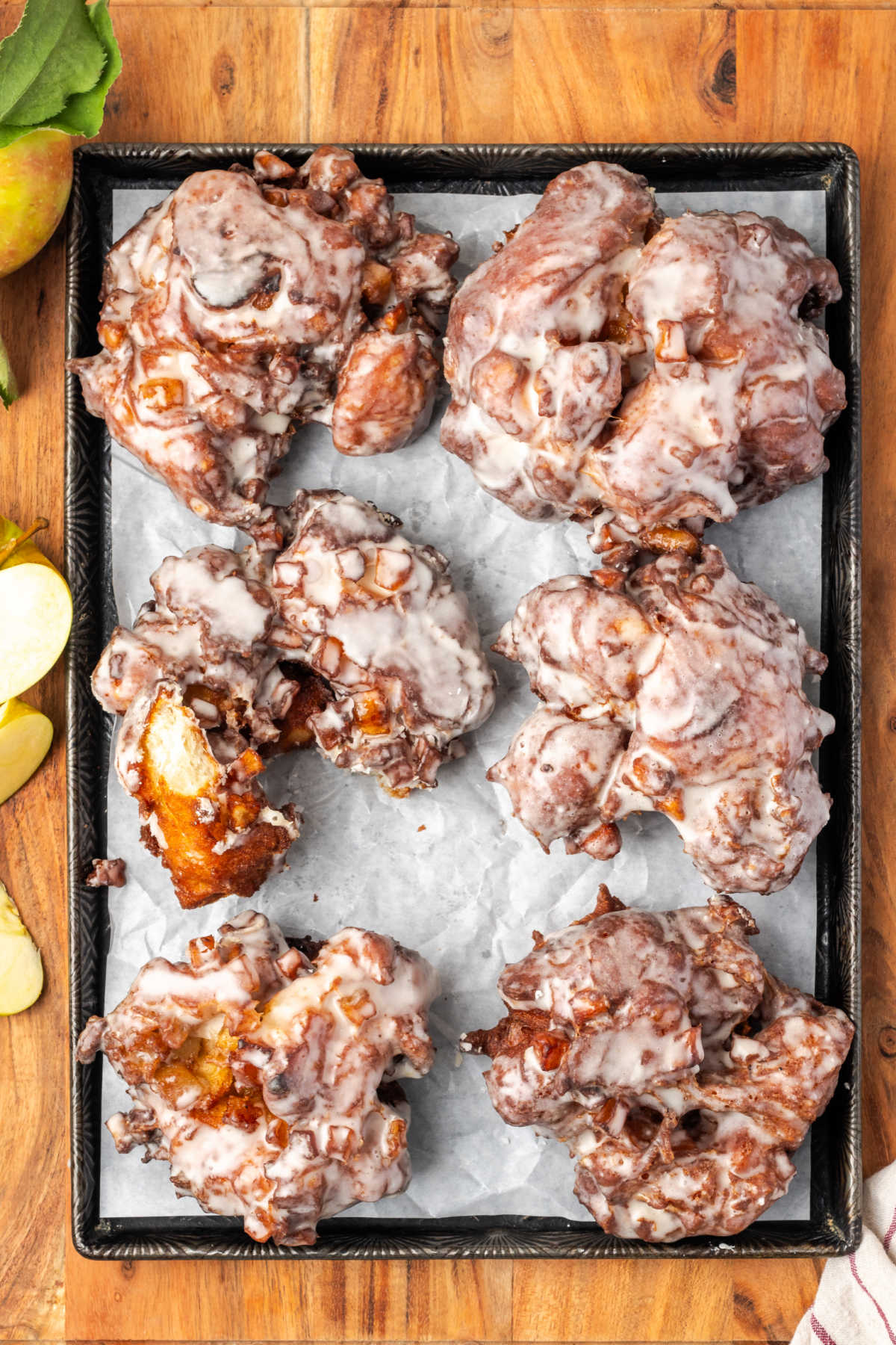 Fried apple fritters with glaze on sheet pan with parchment paper.