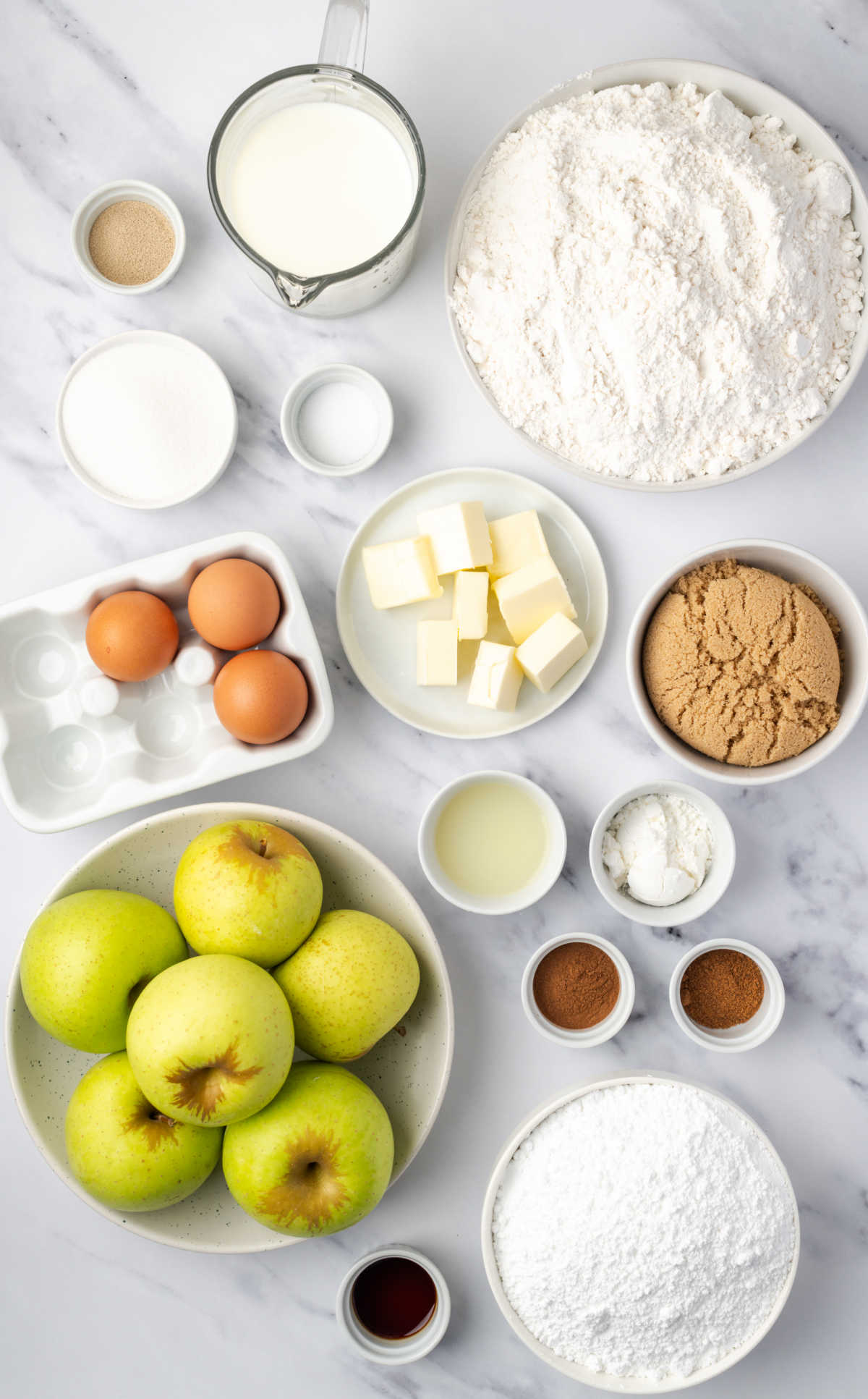 Ingredients in small white bowls for apple fritters on white marble.