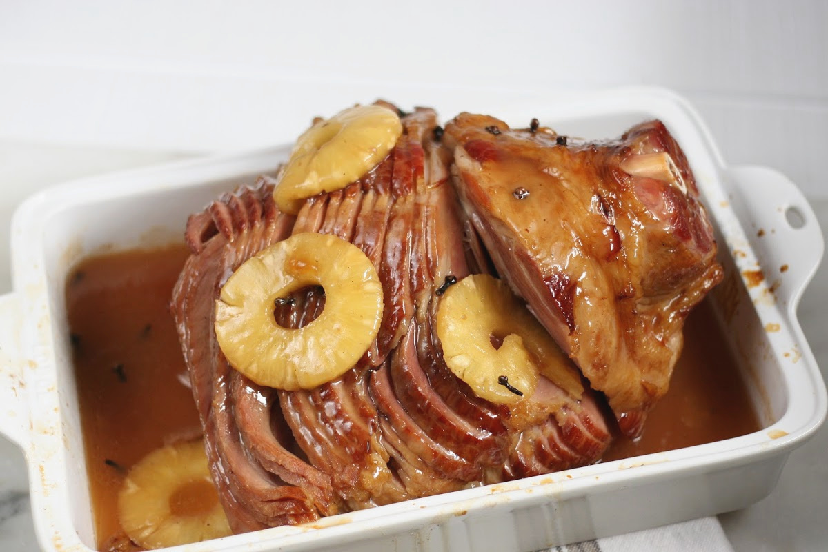 sliced ham with pineapple slices, whole cloves in white rectangle baking dish.