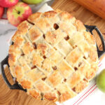 Apple pie with lattice crust in cast iron pie plate, sitting on wooden cutting board.