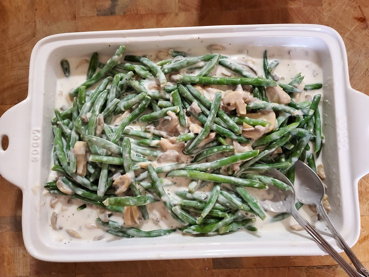 making green bean casserole in a rectangle white ceramic baking dish on butcher block.