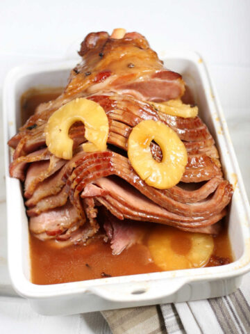 spiral sliced bone-in ham with pineapple slices in white rectangle baking dish.