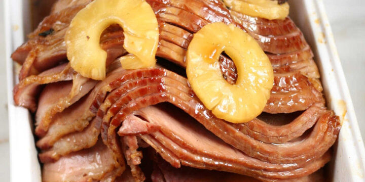 spiral sliced bone-in ham with pineapple slices in white rectangle baking dish.