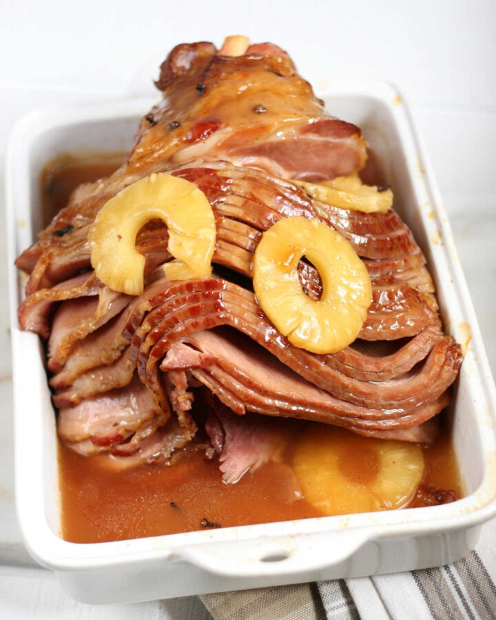 spiral sliced bone-in ham with pineapple slices in white rectangle baking dish.
