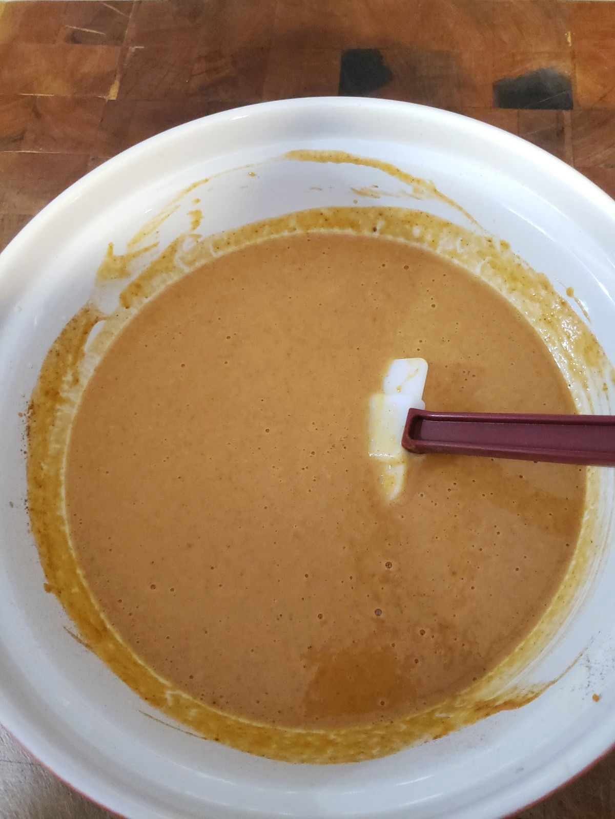 pumpkin pie mixture in a ceramic bowl, rubber spatula in bowl.