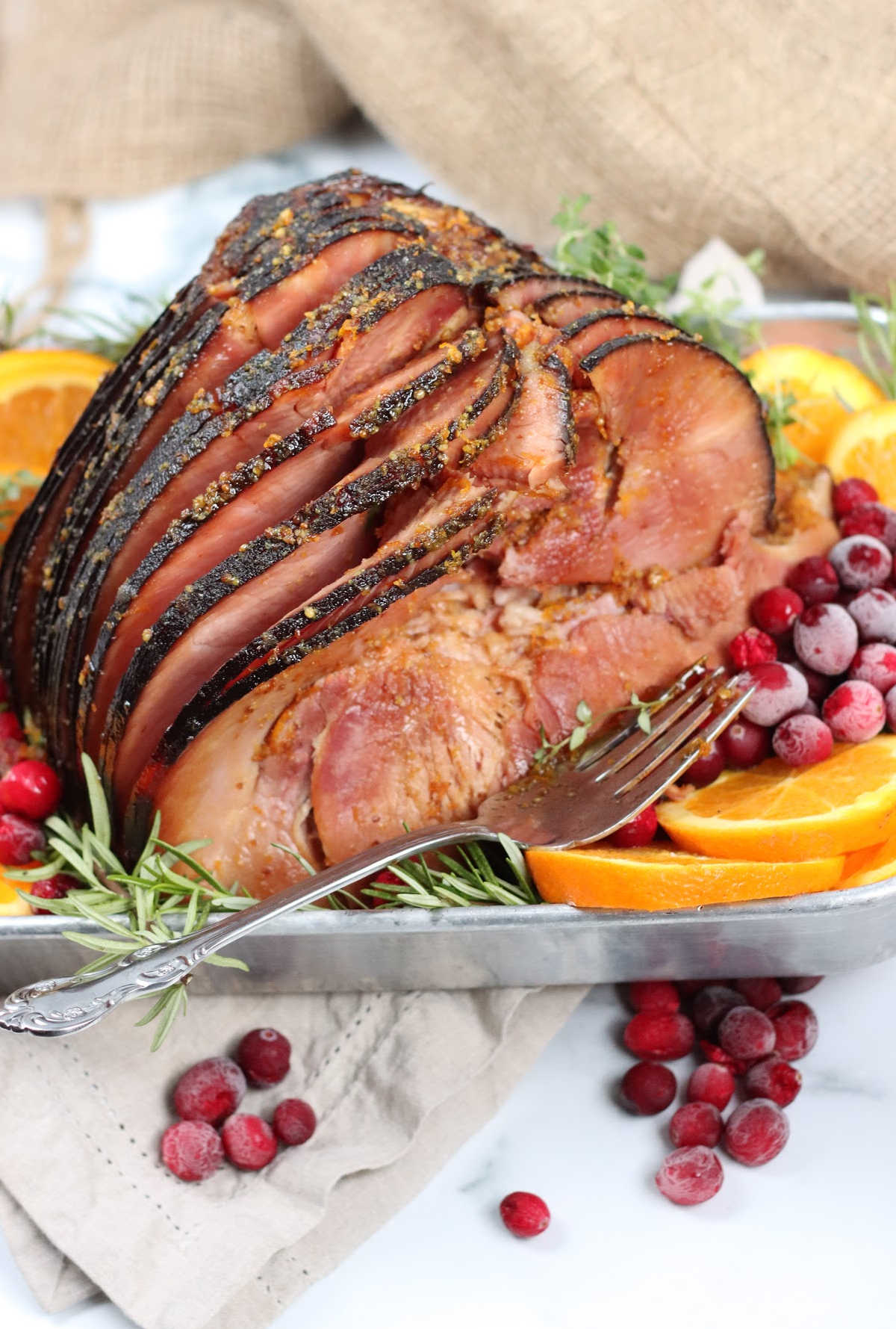 glazed ham spiral cut in metal baking pan, orange slices, cranberries, fresh herbs.
