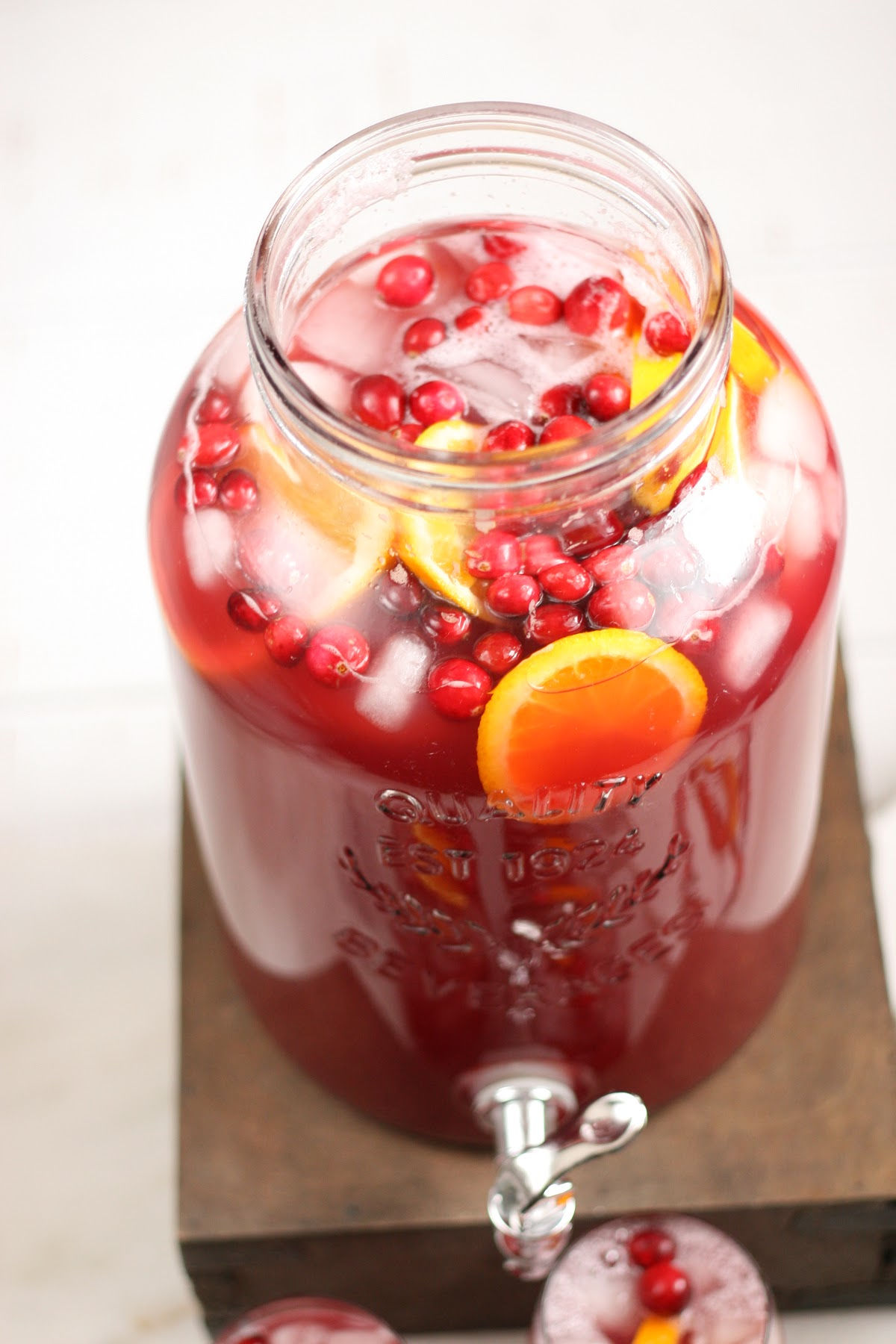 Overhead shot of clear glass drink dispenser of holiday punch, cranberries, orange slices and ice cubes.