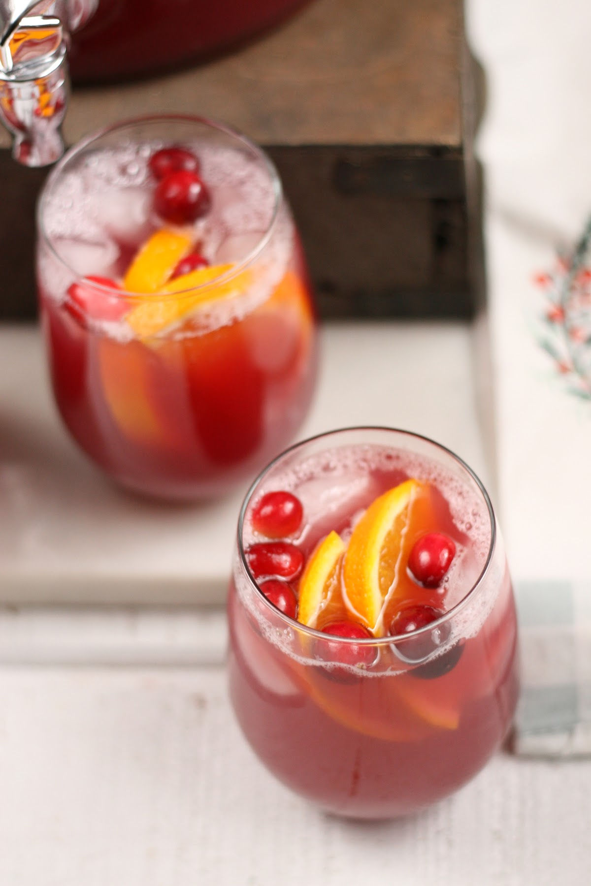 Two stemless glasses of holiday punch, cranberries and orange slices, ice cubes in glassses.