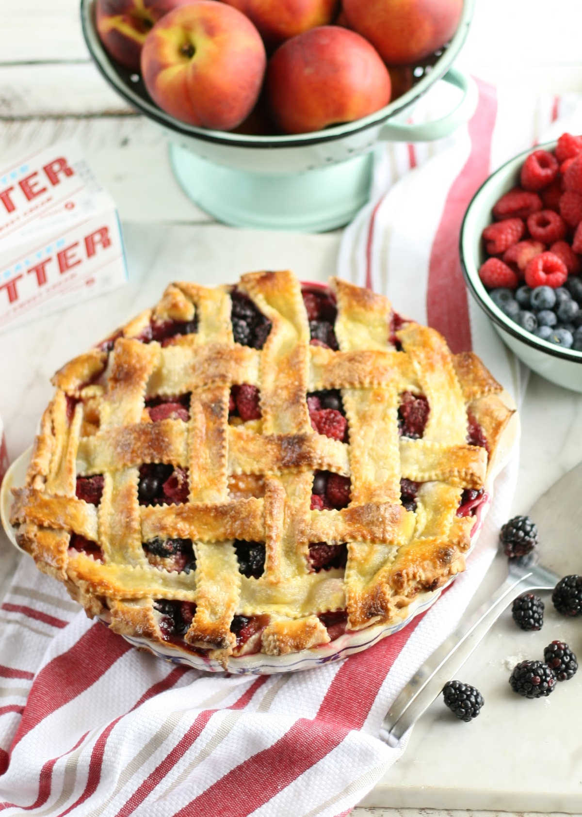 close up of triple berry pie with lattice crust on white and red striped kitchen cloth.