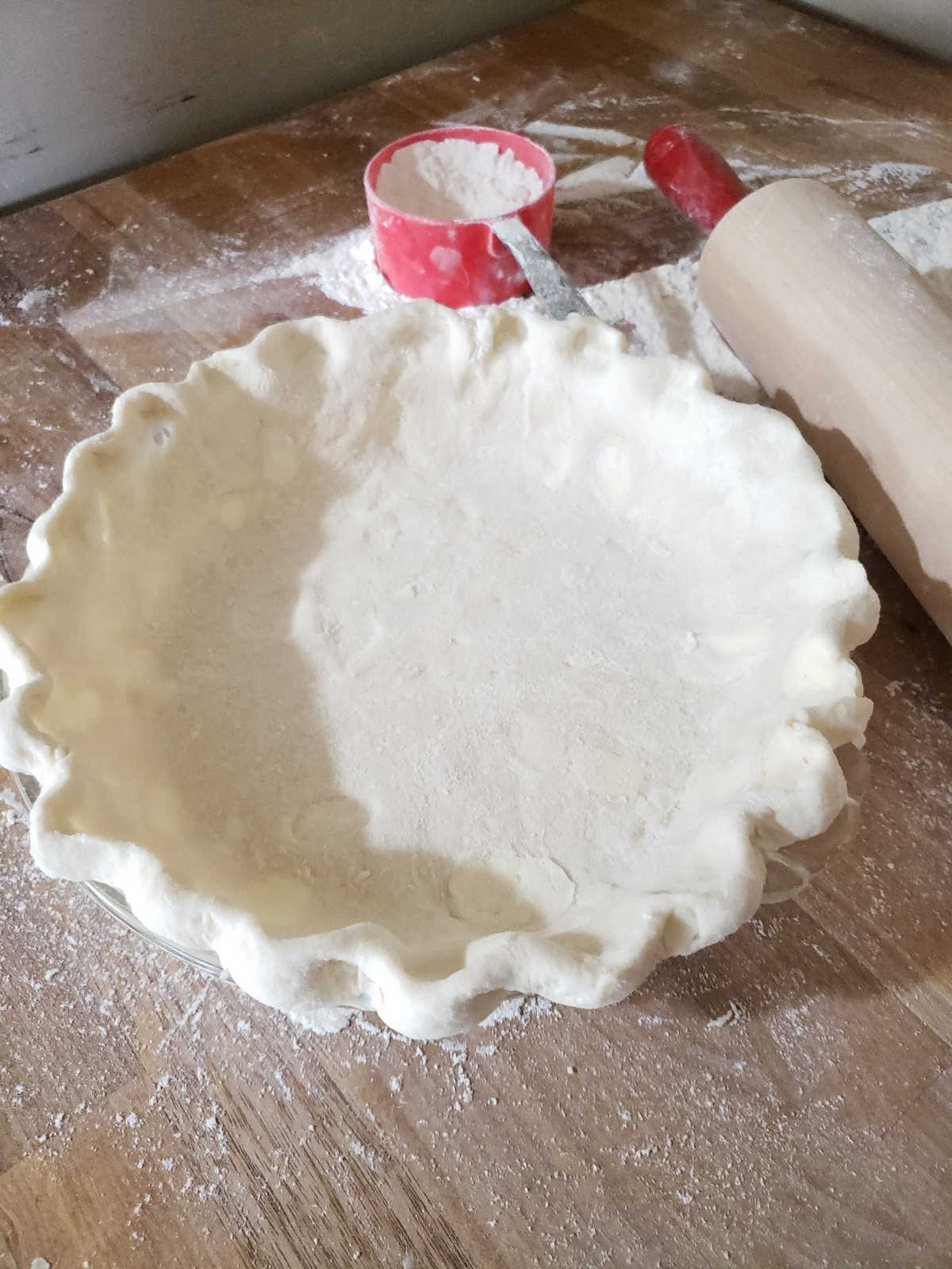 unbaked pie crust in glass pie dish on butcher block.