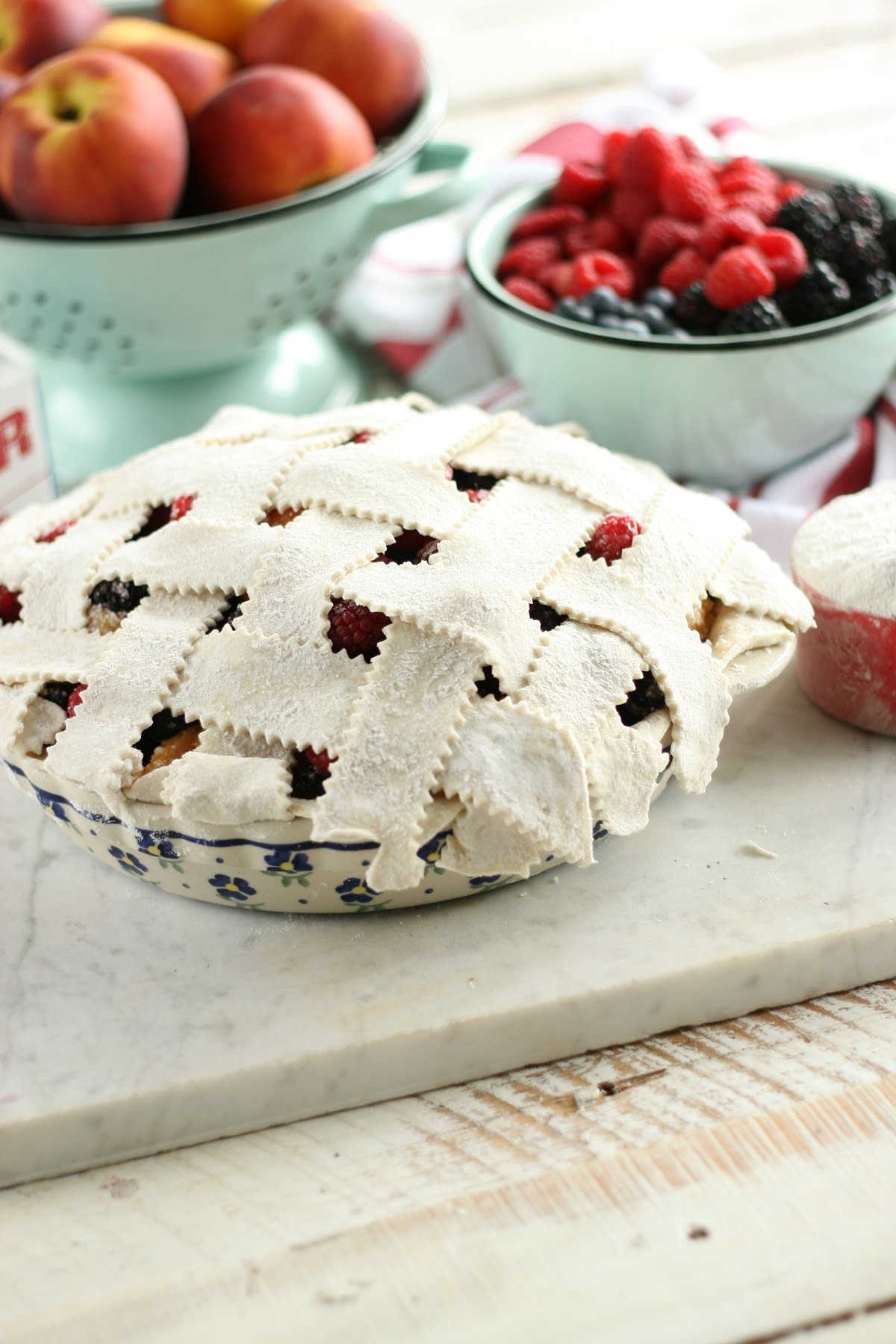 weaving lattice crust on berry pie in blue floral pie plate.