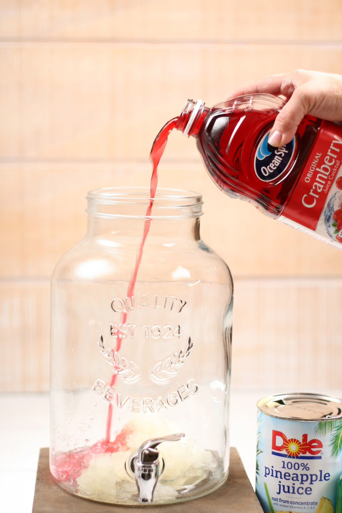 Pouring cranberry juice into clear glass drink dispenser.