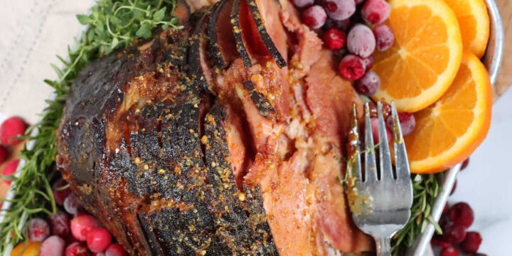 spiral cut ham in metal baking pan, orange slices, cranberries, fresh herbs, on cutting board.