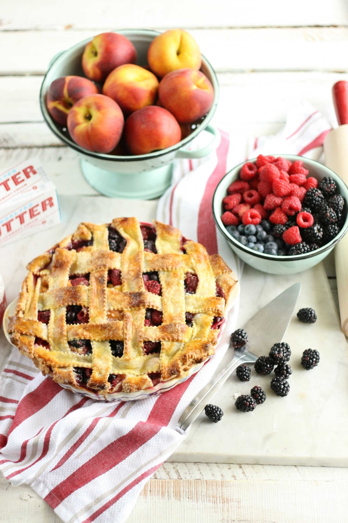 berry pie with lattice crust in blue floral pie dish, fruit in mint green enamelware strainer.