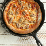 Pizza in cast iron skillet with golden browned crust and cheese.