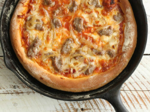 Pizza in cast iron skillet with golden browned crust and cheese.