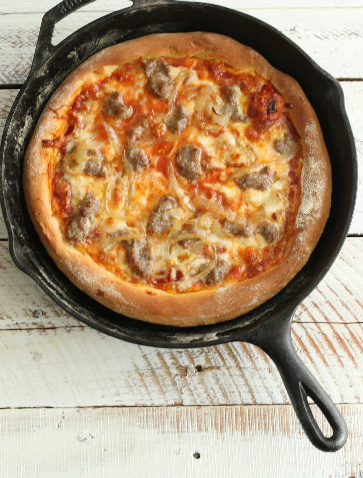 Pizza baked in a cast iron skillet with golden brown cheese and sausage pieces.