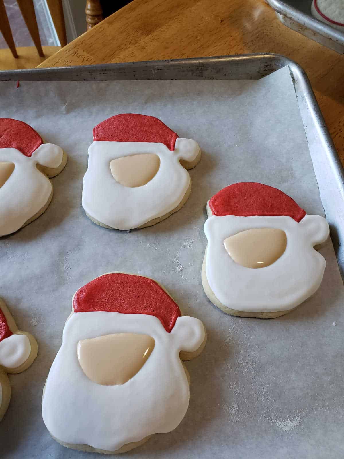 Santa faces sugar cookies with royal icing drying on sheet pan.