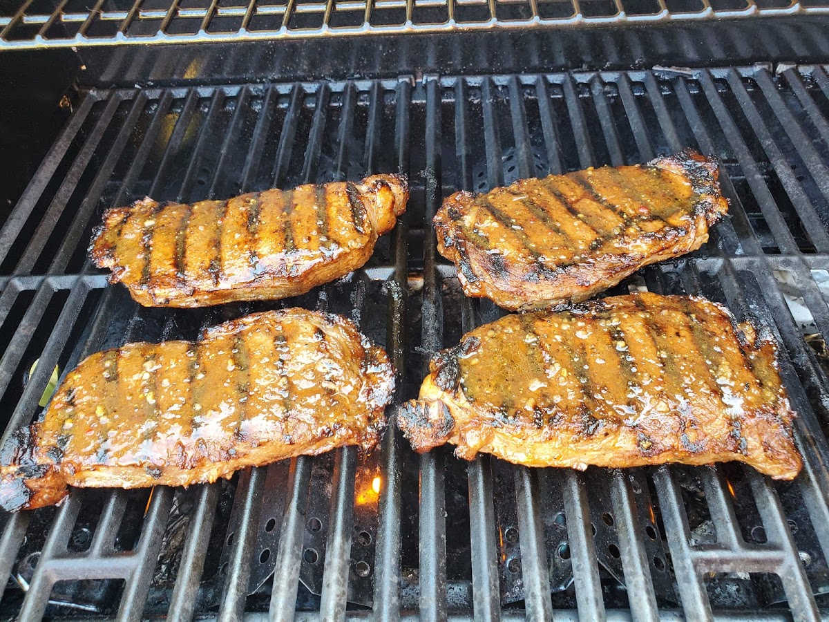 Grilled steak on the grill with flames below grates.