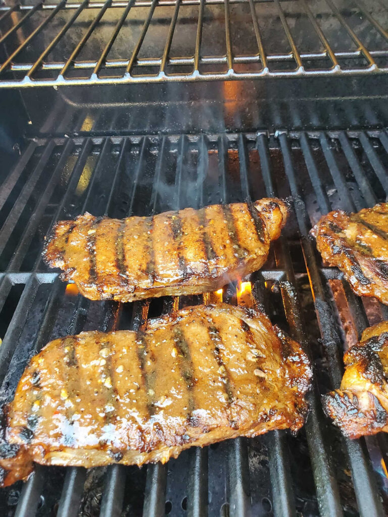 Steak grilling on grill with deep grill marks and marinade on top.