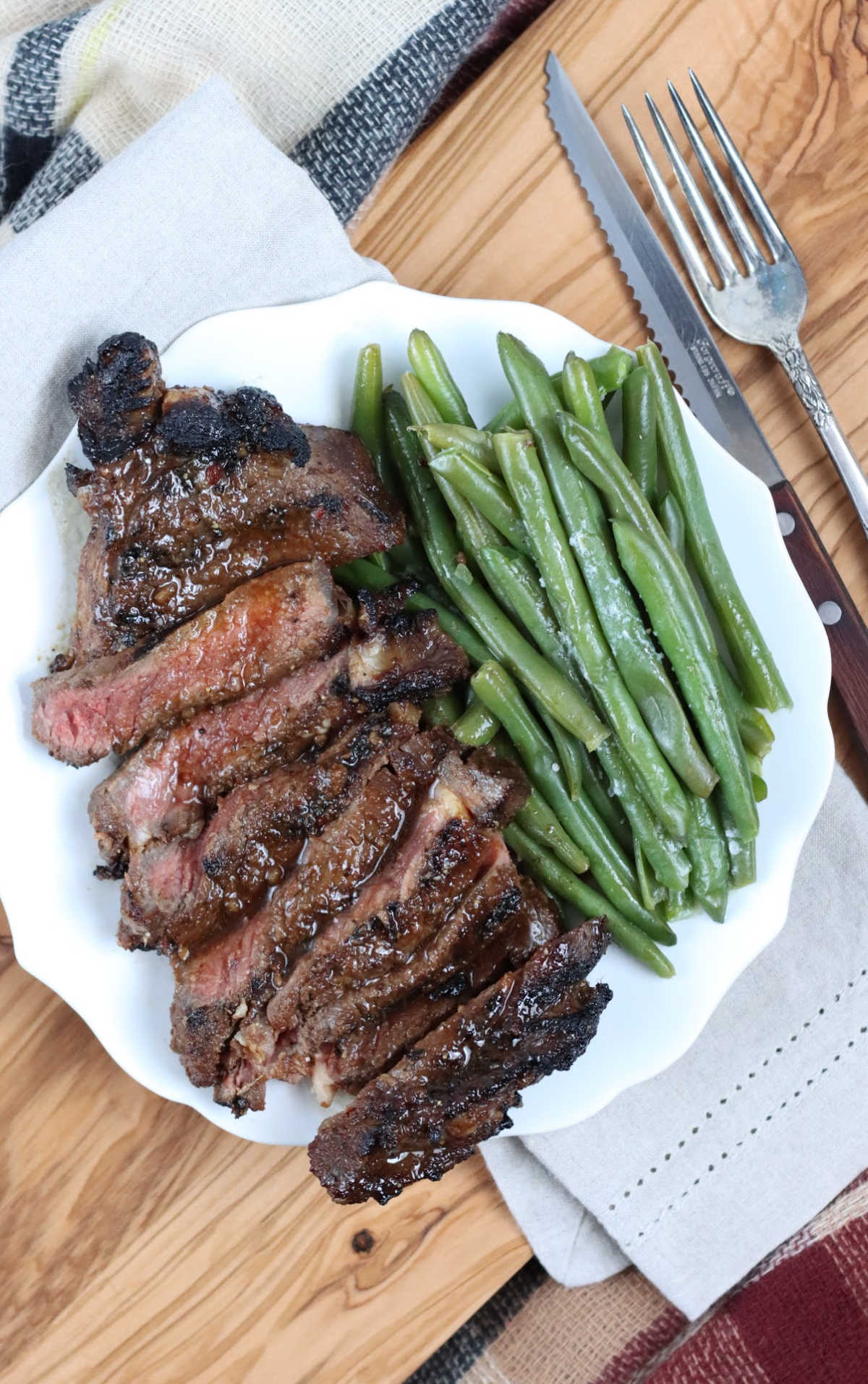 Grilled steak sliced on small white scalloped plate, fresh green beans to side.