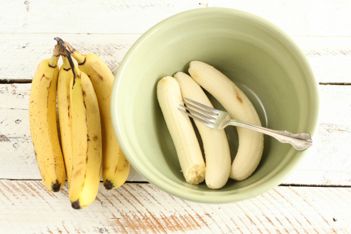 Mint green color ceramic mixing bowl with ripe bananas and fork, ripe bananas to left.