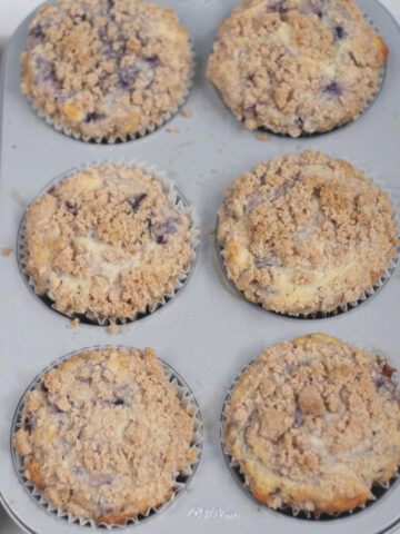 Blueberry muffins with crumb topping in a muffin pan.