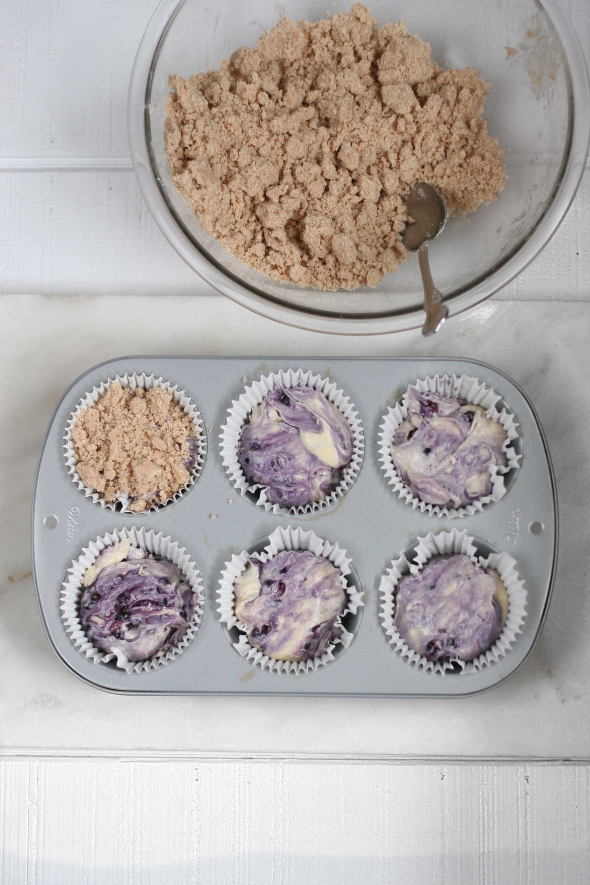Jumbo muffin pan with white paper liners filled with blueberry muffin batter.