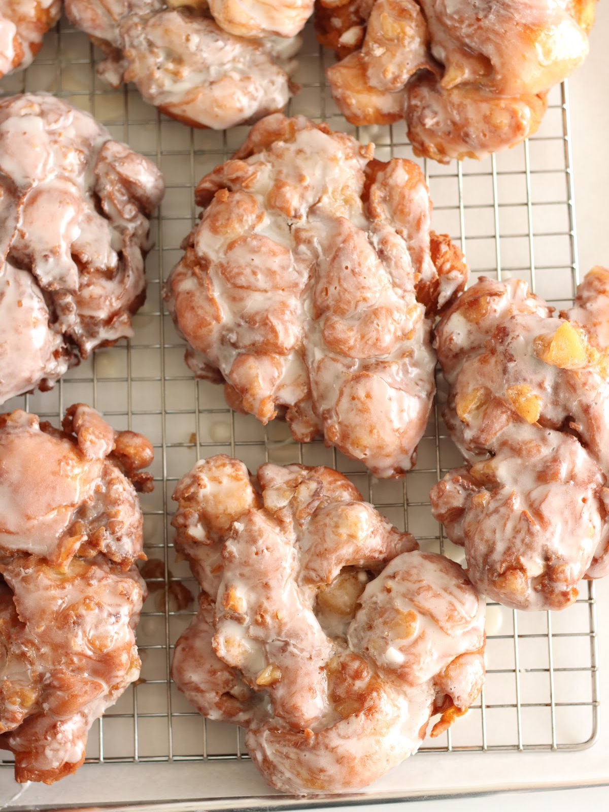 Apple fritters with icing drying on metal baking rack.