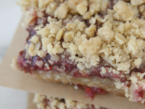Raspberry oatmeal bars stacked on each other with brown parchment in between.