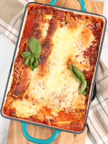 Lasagna in teal green baking dish with handles, golden browned cheese.