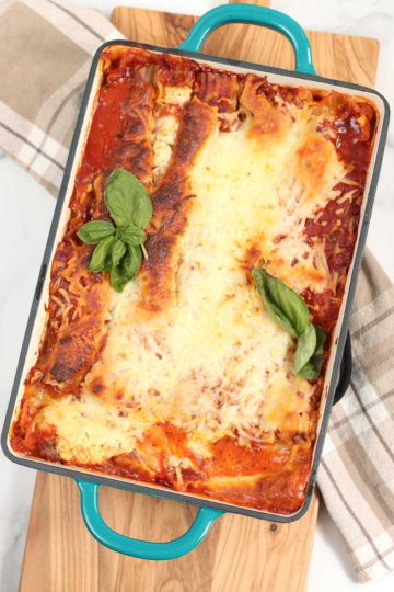 Lasagna in teal green baking dish with handles, golden browned cheese.