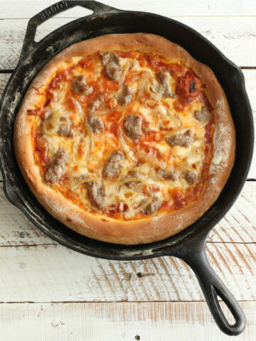 Homemade pizza with golden browned crust and cheese in cast iron skillet.