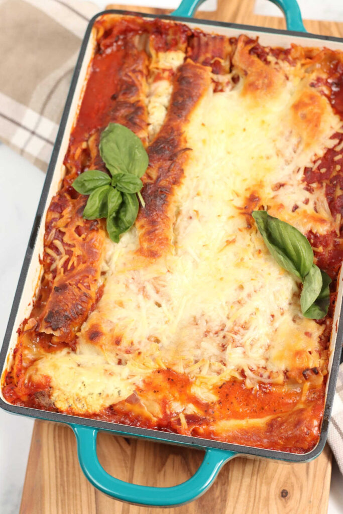 Lasagna in a teal color dual handle rectangle baking dish.