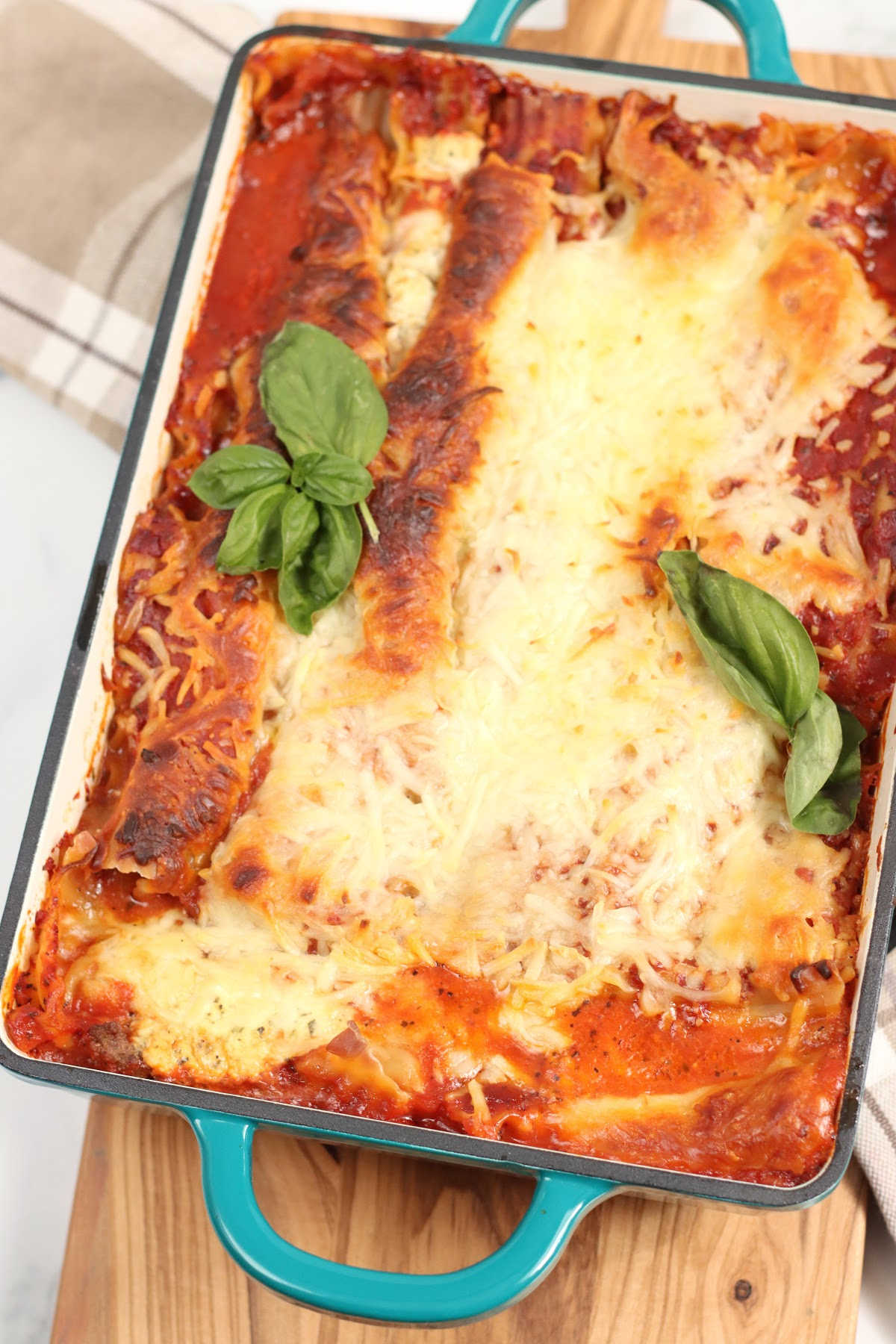 Lasagna with golden browned crust in teal green baking pan with two handles.