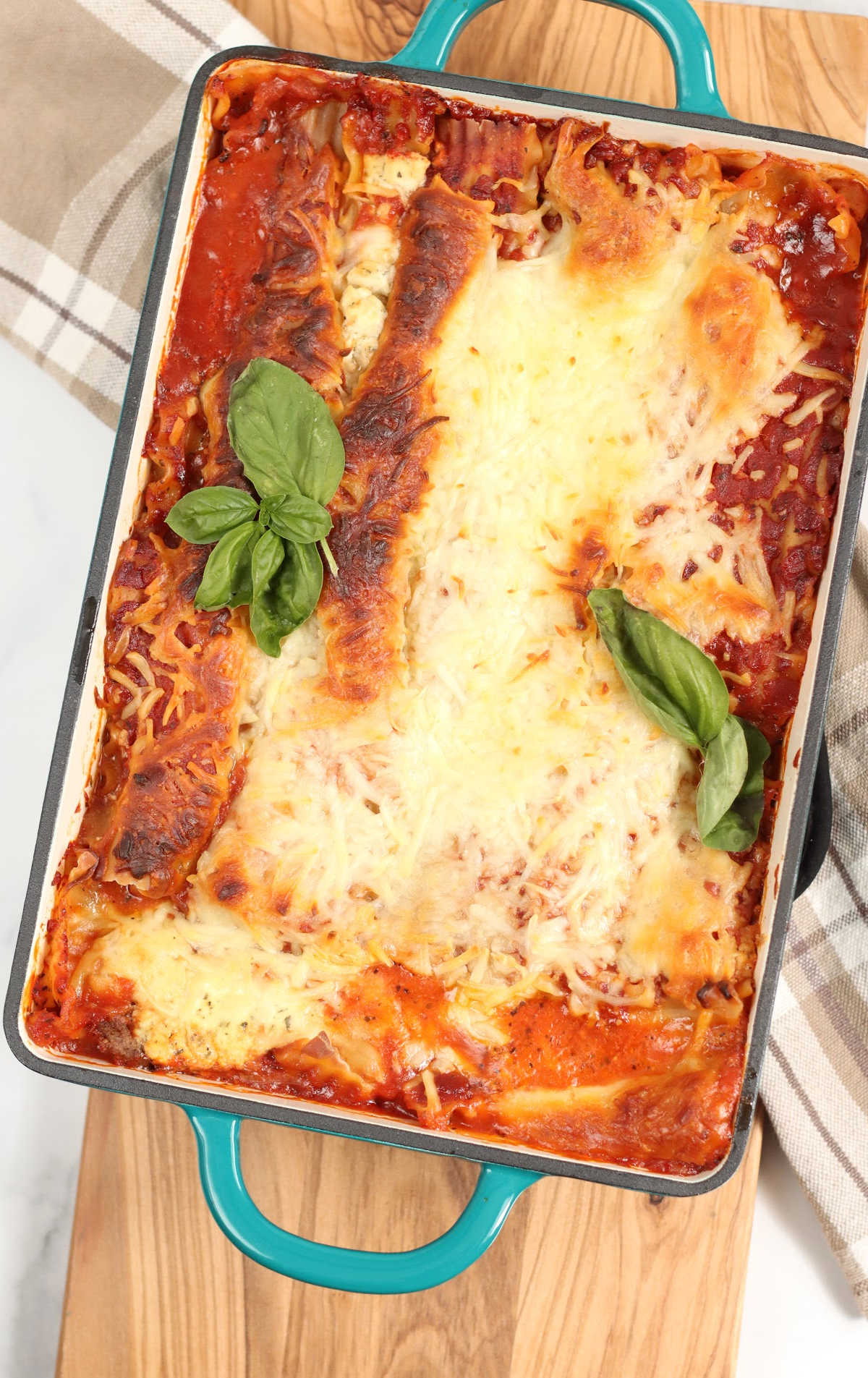 Meat lasagna with golden browned cheese in teal cast iron rectangle baking pan.