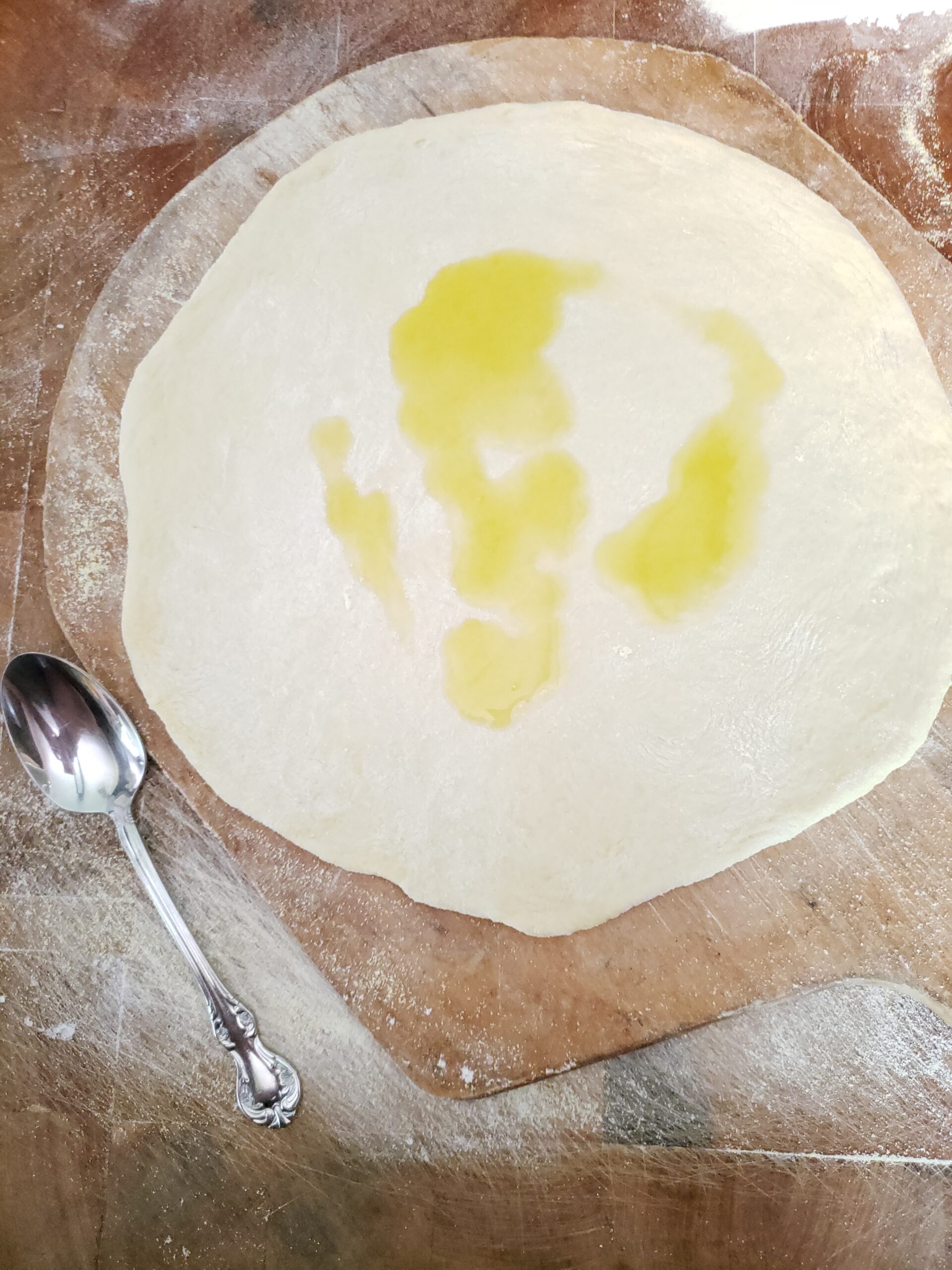 Pizza dough on wooden pizza paddle with olive oil on dough.