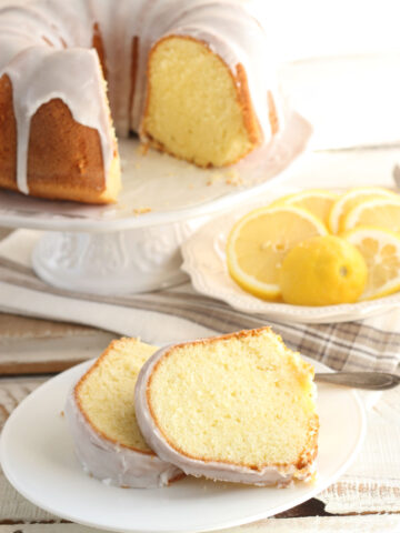 Lemon Bundt cake on white footed cake dish, two slices on small white plate.