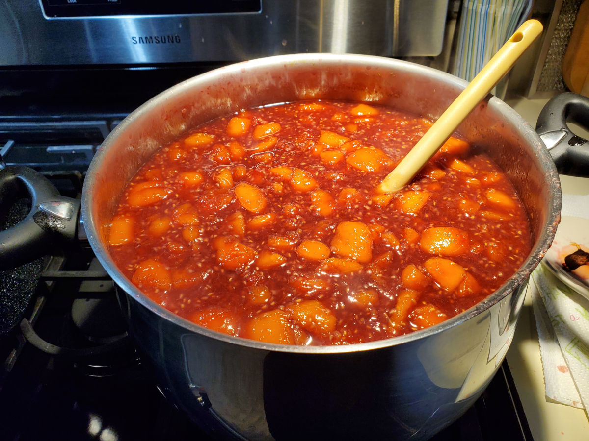 Big pot of raspberry peach jam cooking on the stove.