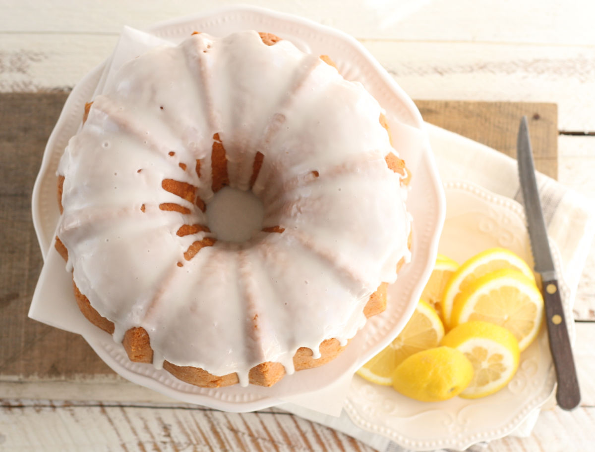 Overhead shot of lemon Bundt cake with icing, lemon slices on small white plate with knife.