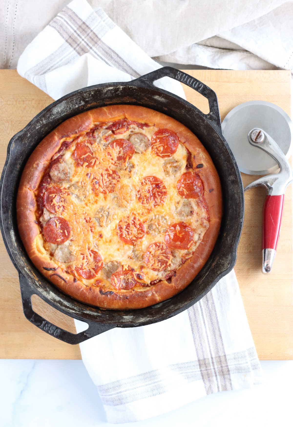 Homemade pizza in a dual handle cast iron skillet with pepperoni and golden brown cheese.
