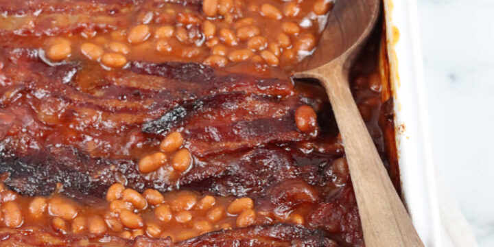 Baked beans in white rectangle baking dish, wooden spoon in dish.