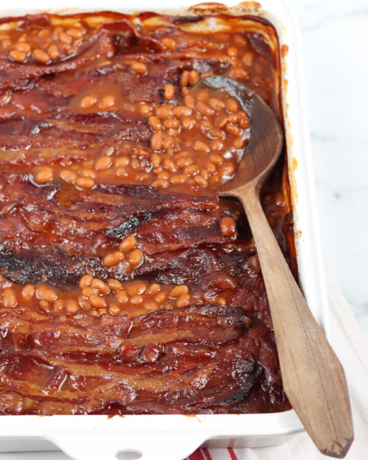 Baked beans in white rectangle baking dish, wooden spoon in dish.