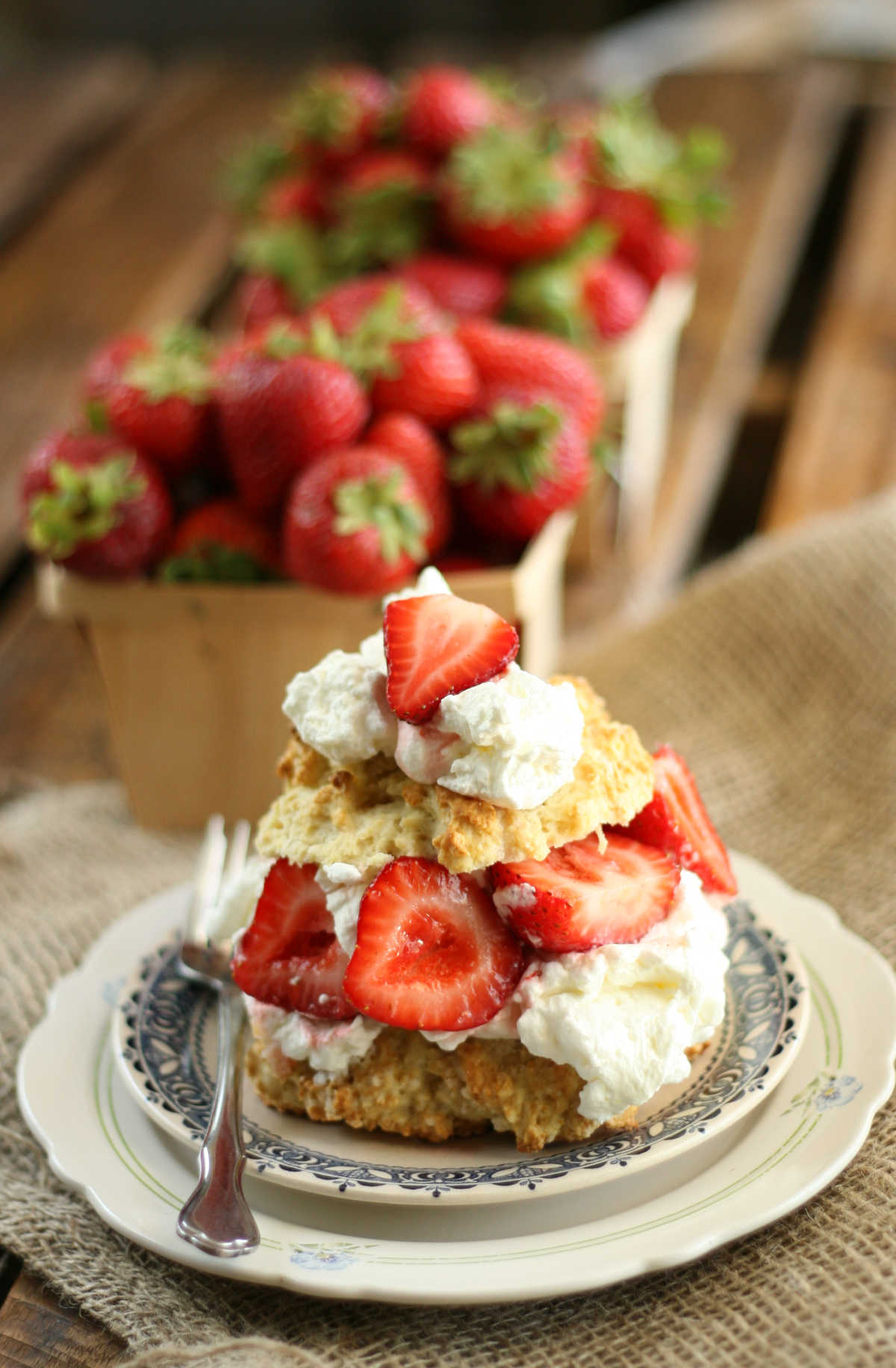 Strawberry shortcake biscuits, fresh strawberries, whipped cream on small white plate.