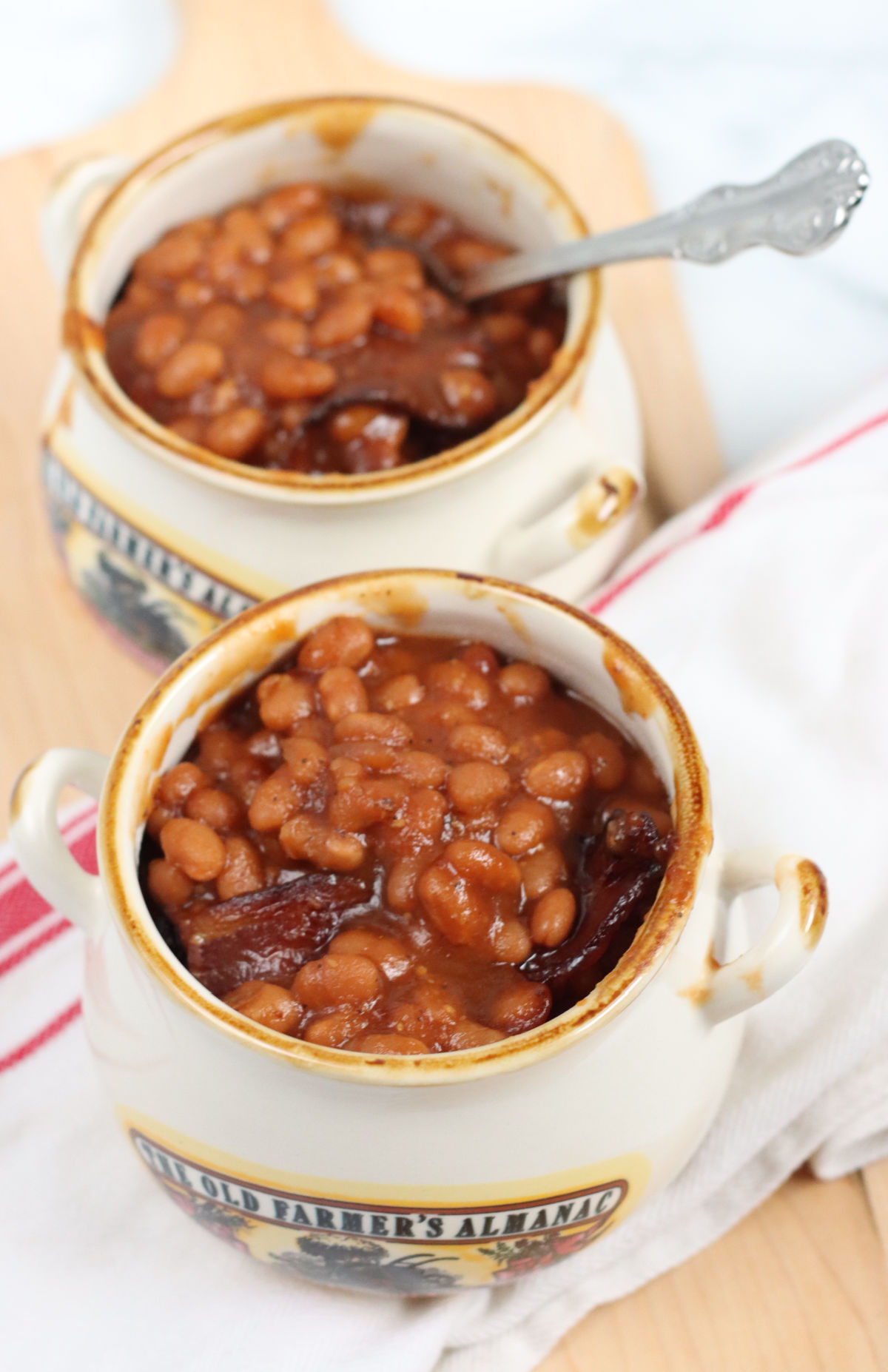 Baked beans in small crocks on wooden cutting board.