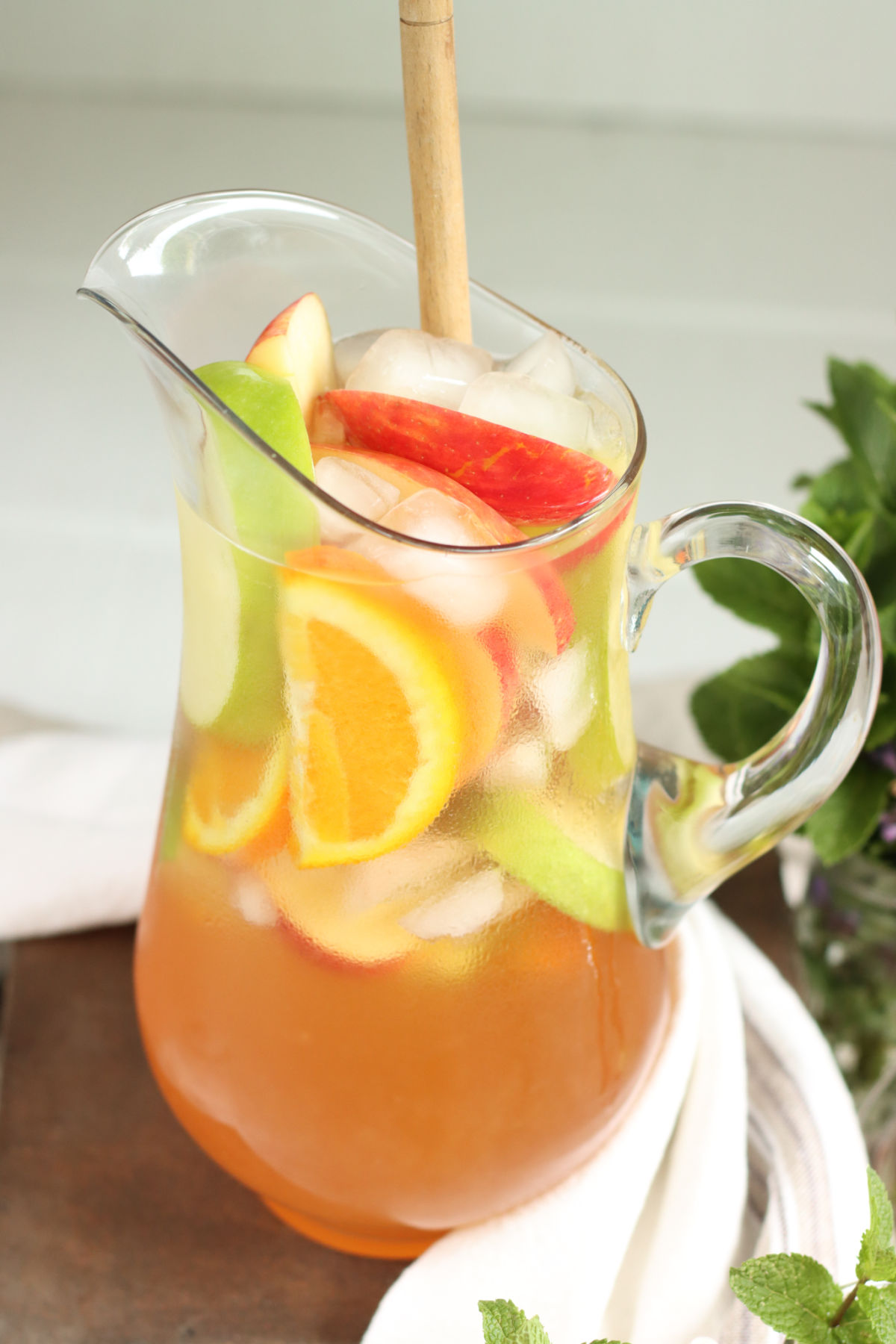 Glass pouring picture with sangria, orange and apple slices, wooden spoon in it.